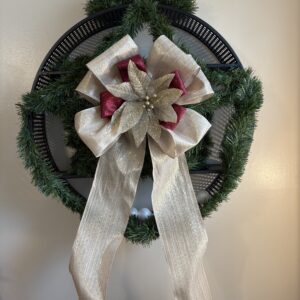 A huge gold and red bow tree topper with a sparkling poinsettia, perfect for Christmas decor. The large gold Christmas bow has long tails and is shown on a wreath.