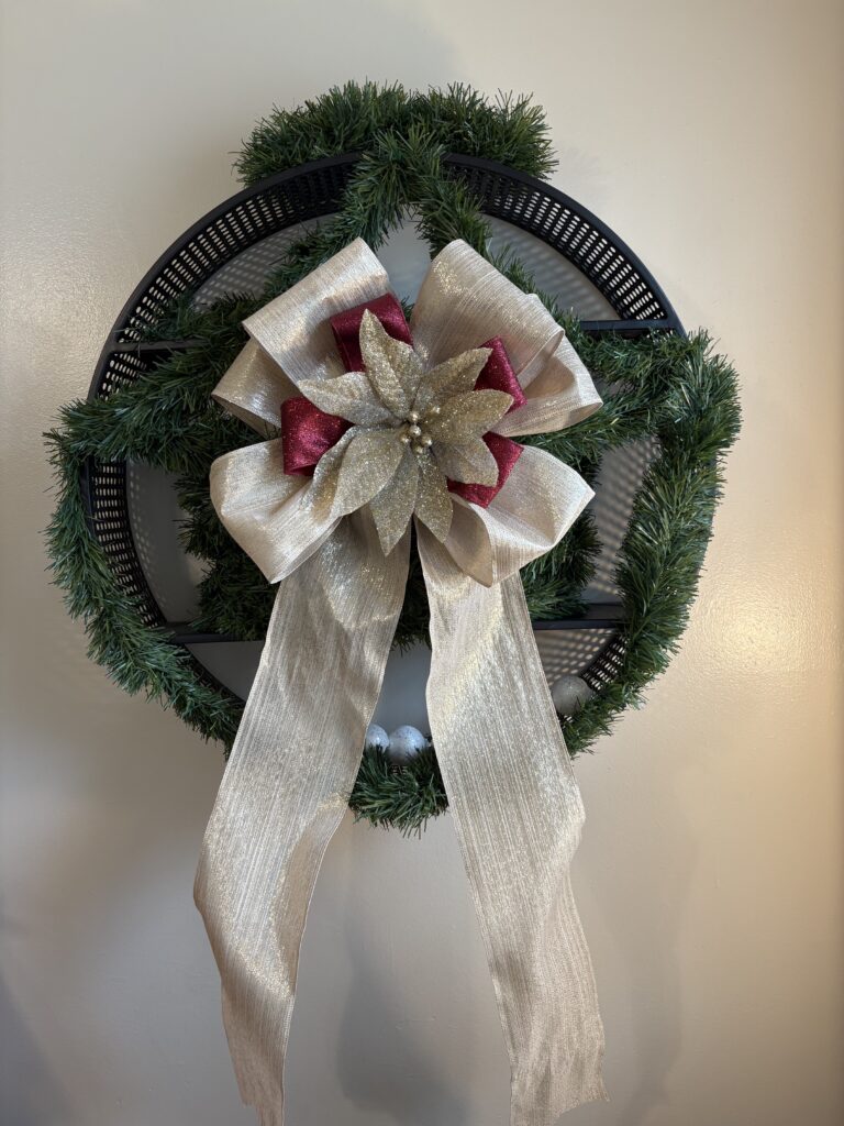 A huge gold and red bow tree topper with a sparkling poinsettia, perfect for Christmas decor. The large gold Christmas bow has long tails and is shown on a wreath.